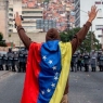 23 January 2019, Venezuela, Caracas: A man wrapped in a flag of Venezuela raises his arms high in front of a number of security forces. In the midst of the escalating political crisis in Venezuela, many people took to the streets. Many states, international organizations and the opposition no longer recognize Maduro as a legitimate head of state. According to observers, his re-election last year did not take place under free and fair conditions. Photo: Rayner Pena/dpa (Photo by Rayner Pena/picture alliance via Getty Images)