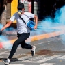 An opposition demonstrator runs with a tear gas canister during clashes with security forces within a protest against the government of President Nicolas Maduro, on the anniversary of the 1958 uprising that overthrew the military dictatorship, in Caracas on January 23, 2019. - Venezuela's National Assembly head Juan Guaido declared himself the country's "acting president" on Wednesday during a mass opposition rally against leader Nicolas Maduro. (Photo by Federico Parra / AFP)        (Photo credit should read FEDERICO PARRA/AFP/Getty Images)